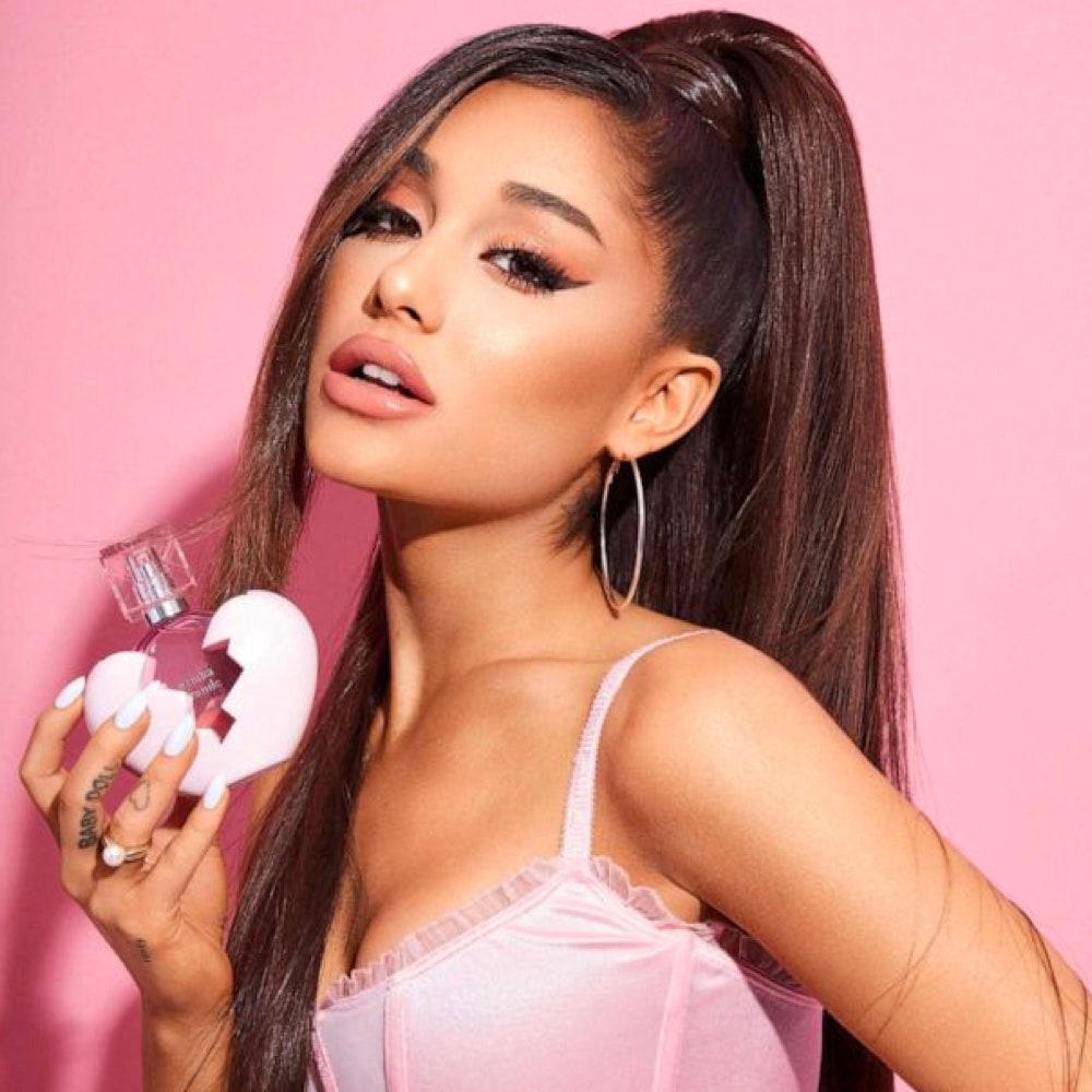 Ariana Grande holding heart shaped perfume bottle on pink background