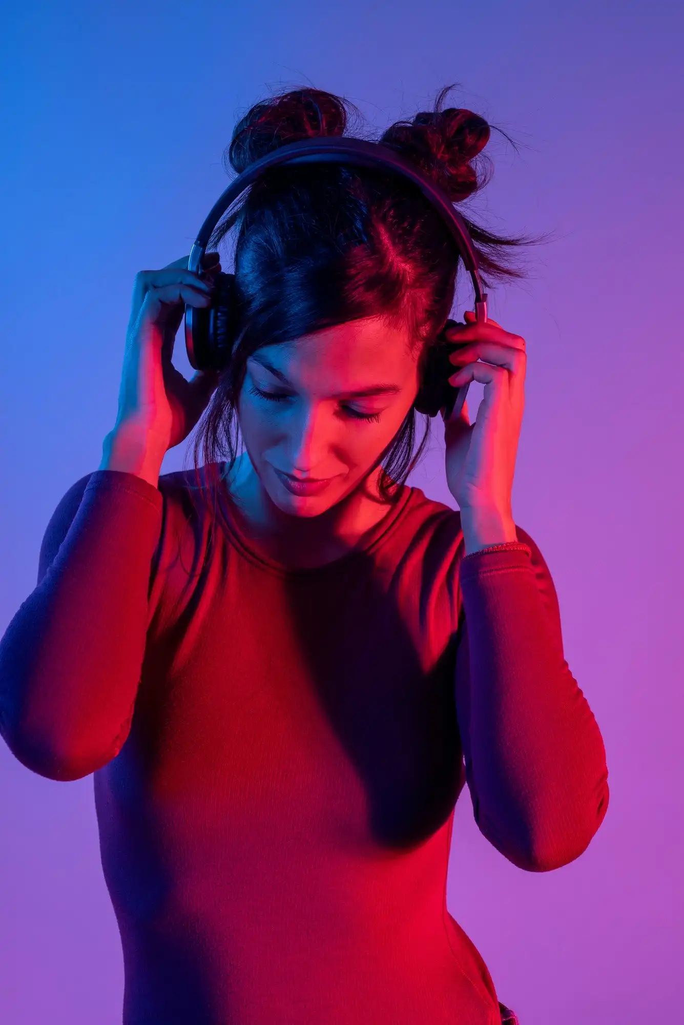 青と赤のライトに照らされたスタジオで音楽を聴くヘッドフォンを持った魅力的な女性