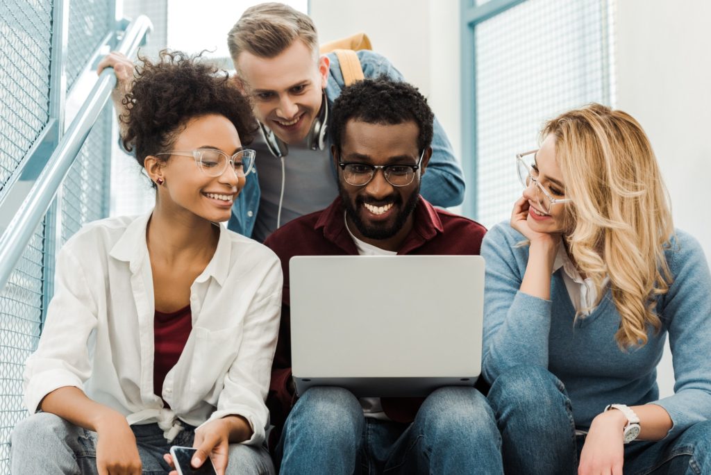 grupa uśmiechniętych wielokulturowych studentów z laptopem na uczelni