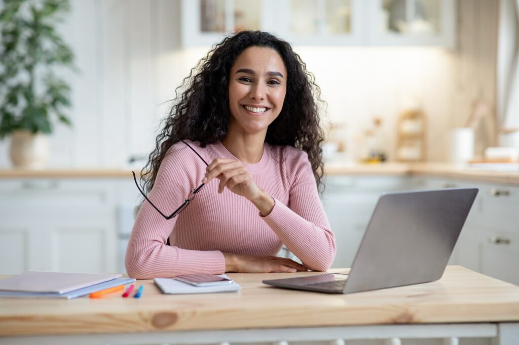 ريادة الأعمال عن بعد. امرأة الألفية السعيدة تجلس على الطاولة مع كمبيوتر محمول في المطبخ