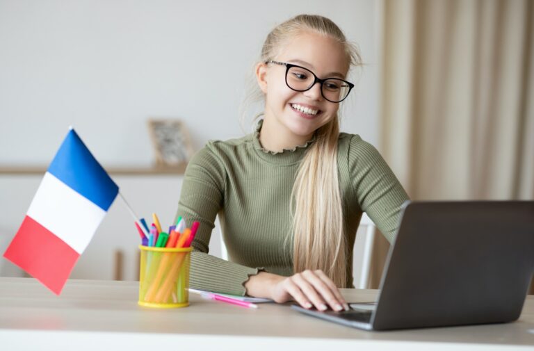 Cheerful girl with flag of France using laptop