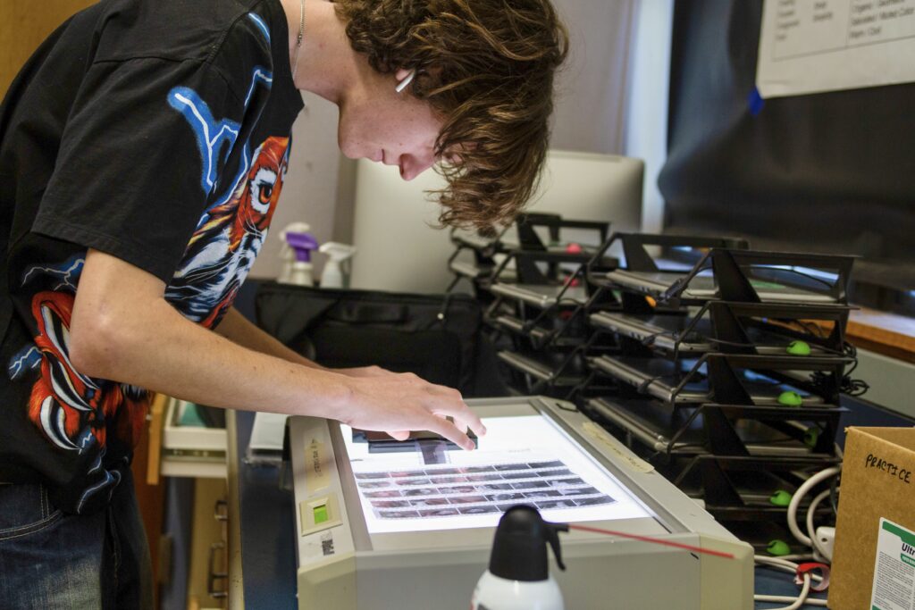 A student leaned over a white flat light, looking at film slides