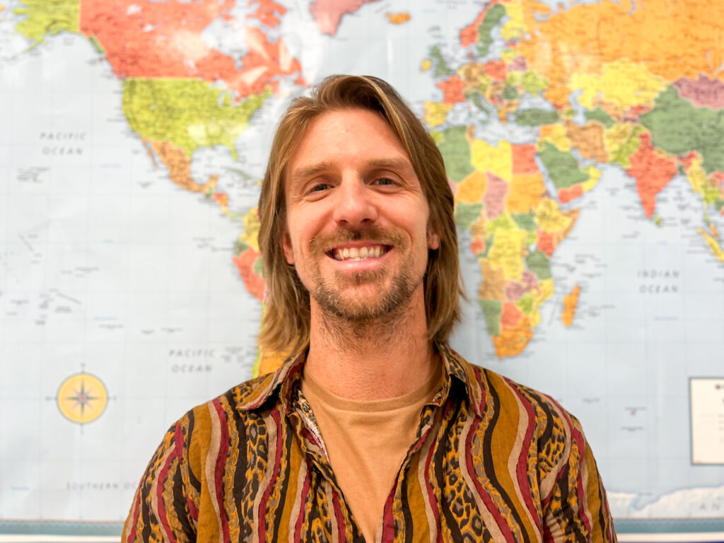 A photo of a substitute teacher with a backdrop of a map of the world.