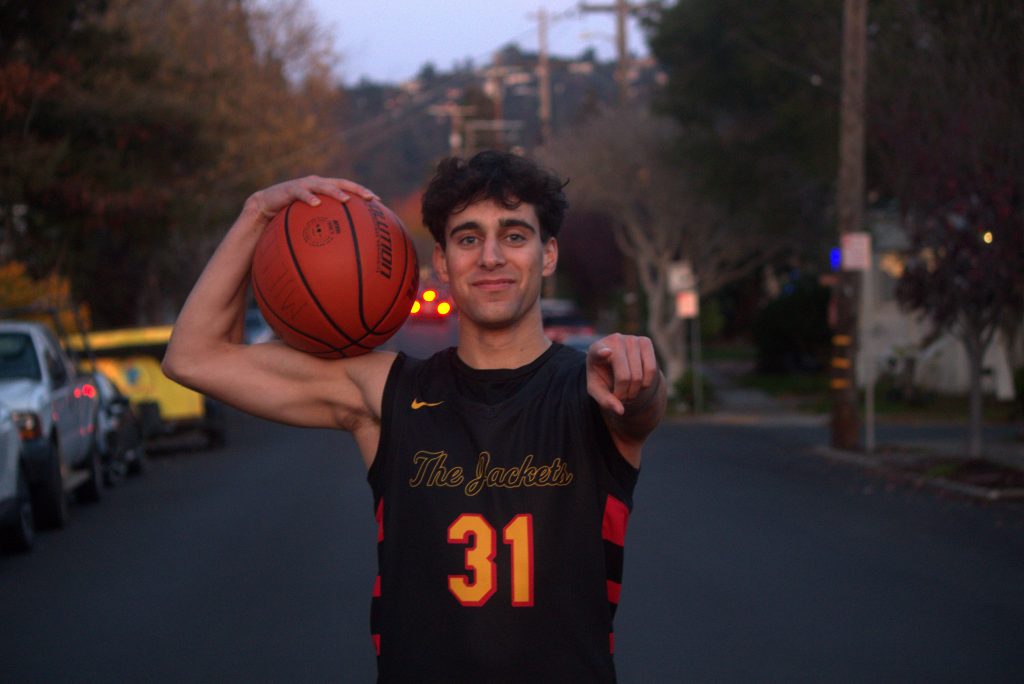 Photo of Ollie Miller holding a basketball and pointing at the camera.