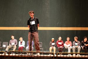 Calder Corson speaks into the microphone on stage at the first annual Spelling Bee.