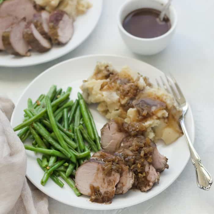 pork tenderloin, green beans, mashed potatoes, gravy on white plate with fork and tan napkin