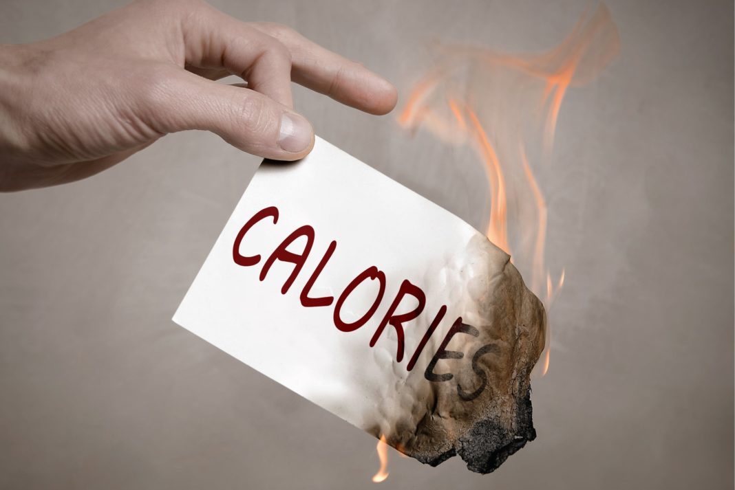 Hand holding a slip of burning paper. The paper has the word 'calories' written on it in red.