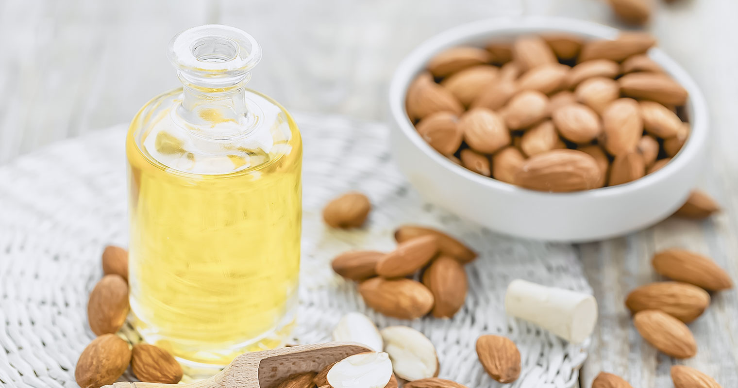 Open bottle of Almond oil and a dish with Almond seeds in the background