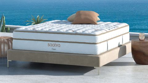 Saatva Classic mattress review: image shows the mattress placed on a beige color bed frame in an outdoor space overlooking a blue ocean