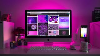 a Mac on a desk showing websites backlit with a pink light