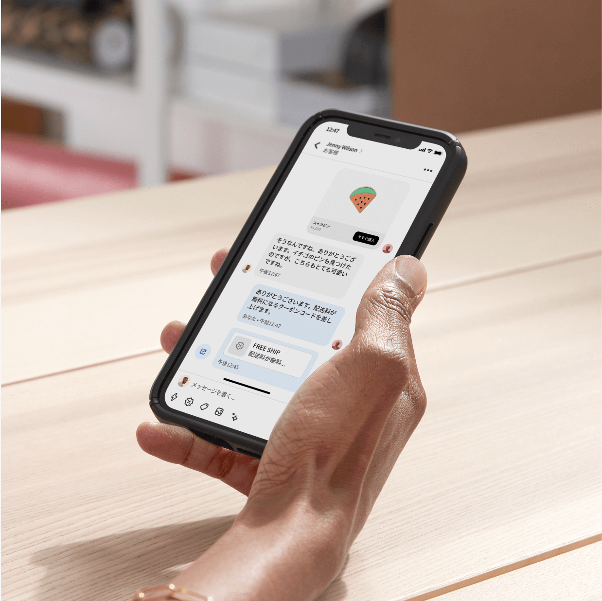 バックオフィスのデスクに座り、Shopify Inboxを使ってモバイルデバイスで顧客とチャットしているビジネスオーナー。購入決定へと導くために、���ャットでクーポンコードを提示している。