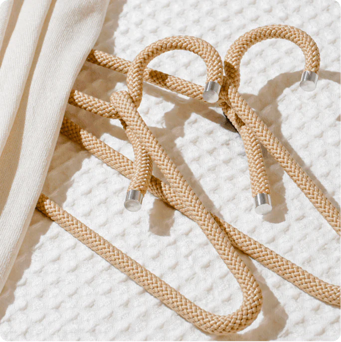 Two cream-colored rope hangers lay on a white textured fabric with a draped piece of apparel covering them.