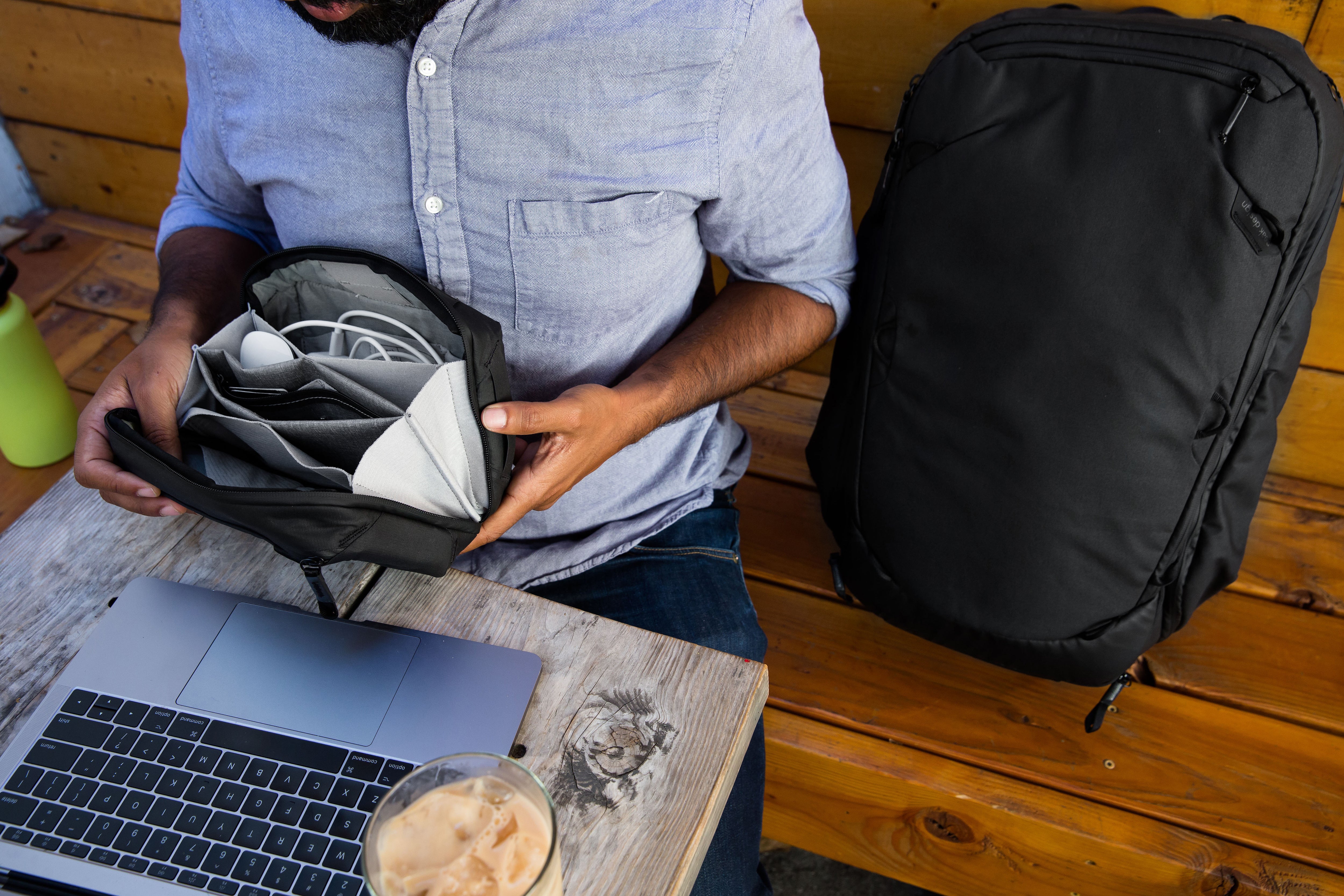 A person in a blue shirt holding an accessories bag from Peak Design while in front of their laptop. 