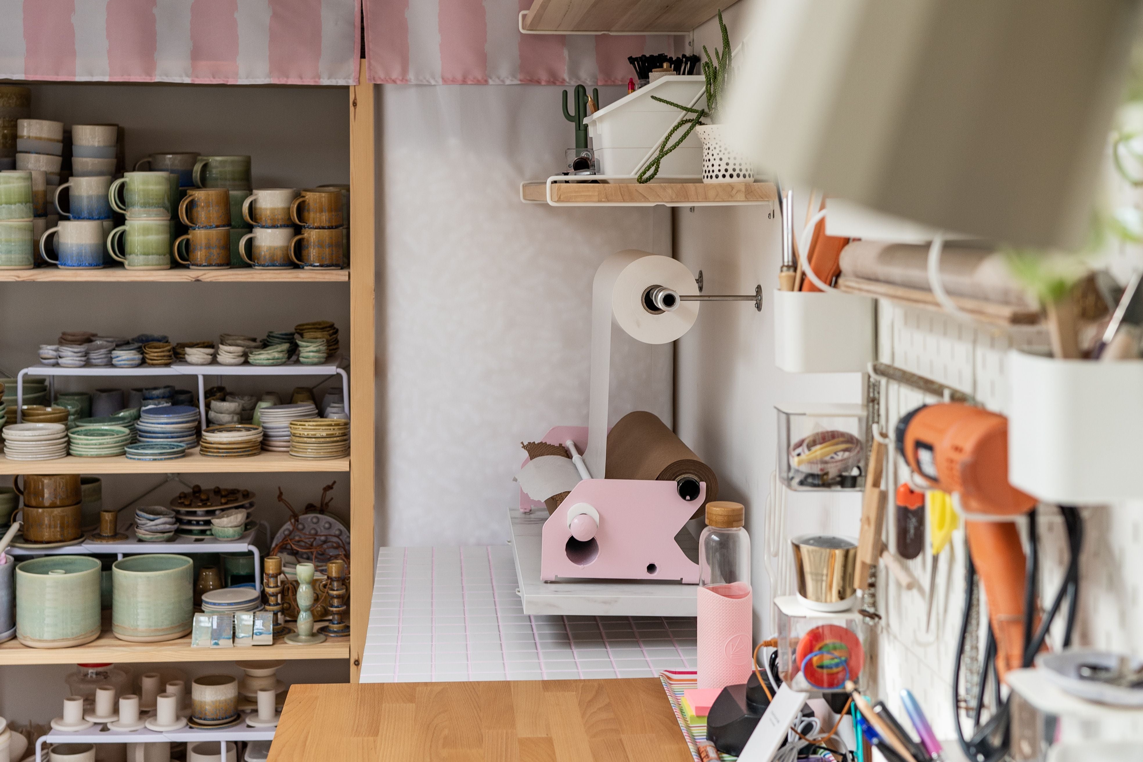 An array of tools hanging on a wall in Raquel’s studio backdropped by ceramics she’s made on a storage shelf. 