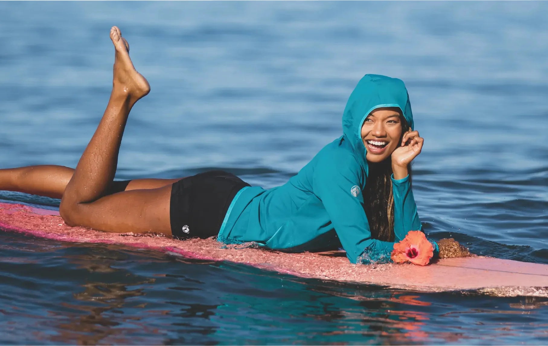 A woman in a hoodie lies on a surf board