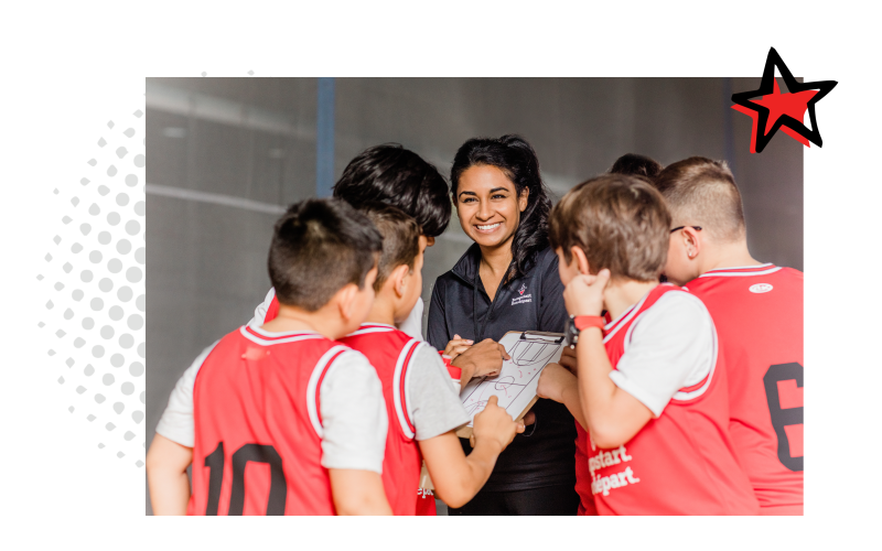 A group of girls stand beside a curling lane as they listen to an instructor who is teaching them about the sport.