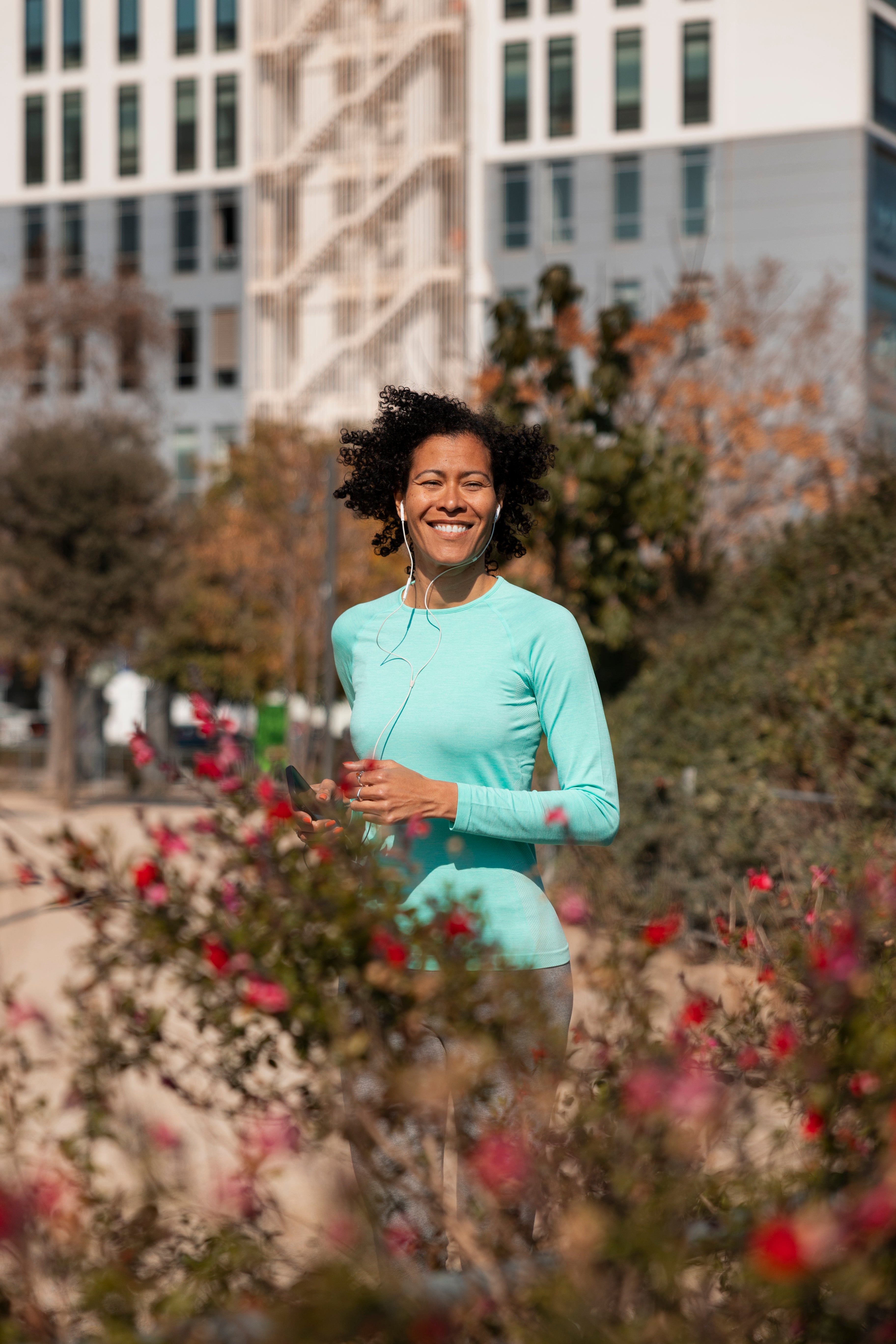 Smiling woman jogging with earphones in an urban park.