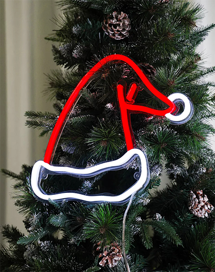 This red neon sign in the shape of a Santa hat hangs on the Christmas tree, enhancing the festive atmosphere.