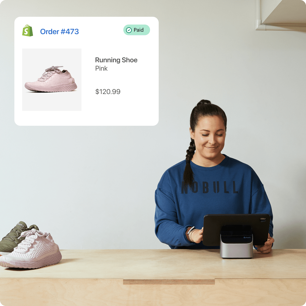 A smiling woman sits at a counter, smiling at a tablet device in front of her. There are two shoes to the left of her, and in the upper left, an order paid confirmation screen with a shoe, a description of “Running shoe - pink” and a cost of $120.99.