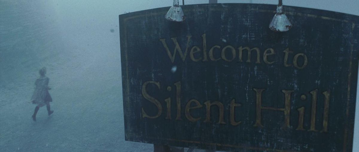 The “Welcome to Silent Hill” sign foregrounds a person walking in the snow.