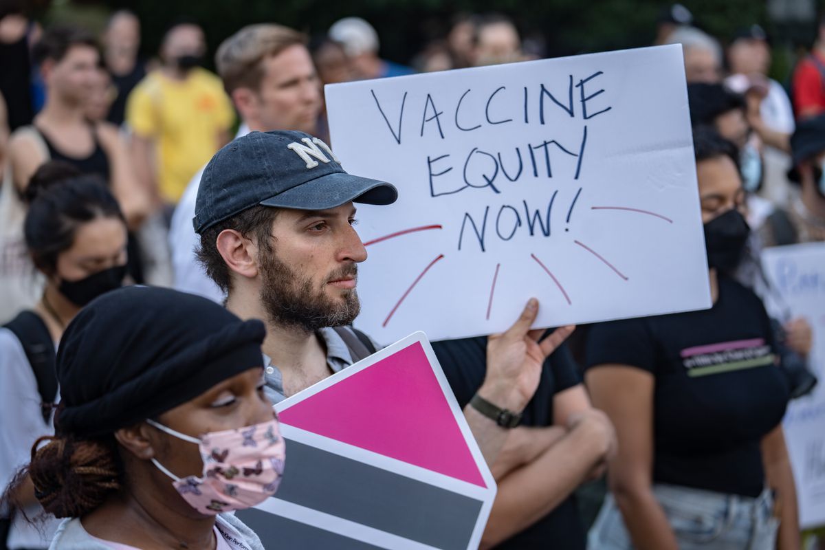 A protester in a crowd holds up a sign that reads, “Vaccine equity now!”