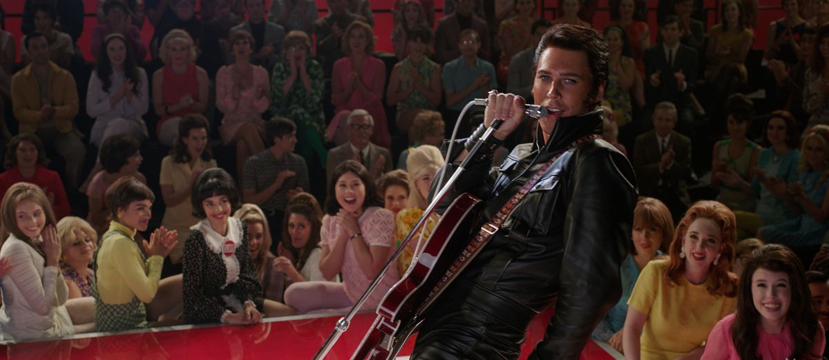 In a leather jumpsuit, surrounded by adoring girls, Elvis sings into the mic.