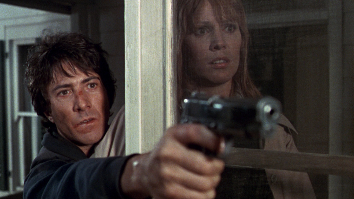 Dustin Hoffman holds a gun around a door frame while Marthe Keller stands on the other side looking concerned in Marathon Man.