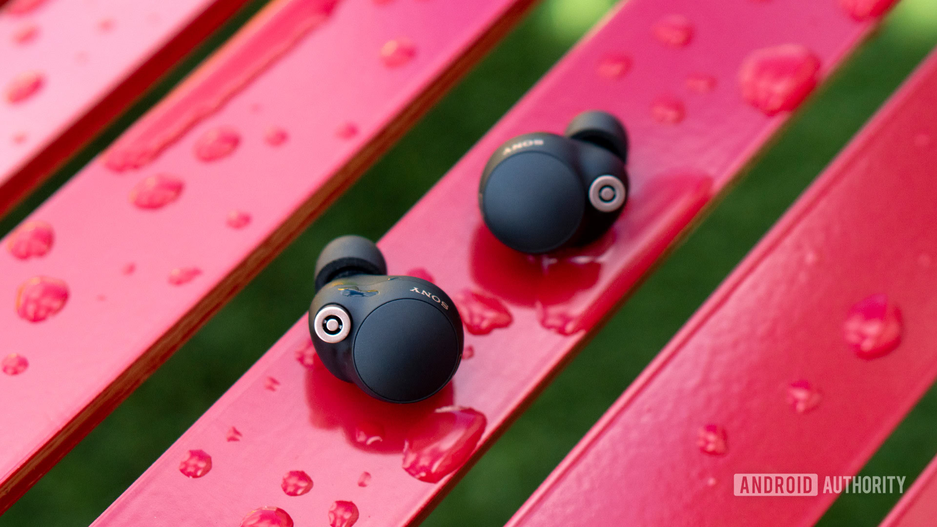 A picture of the Sony WF-1000XM4 earbuds on a wet red bench.