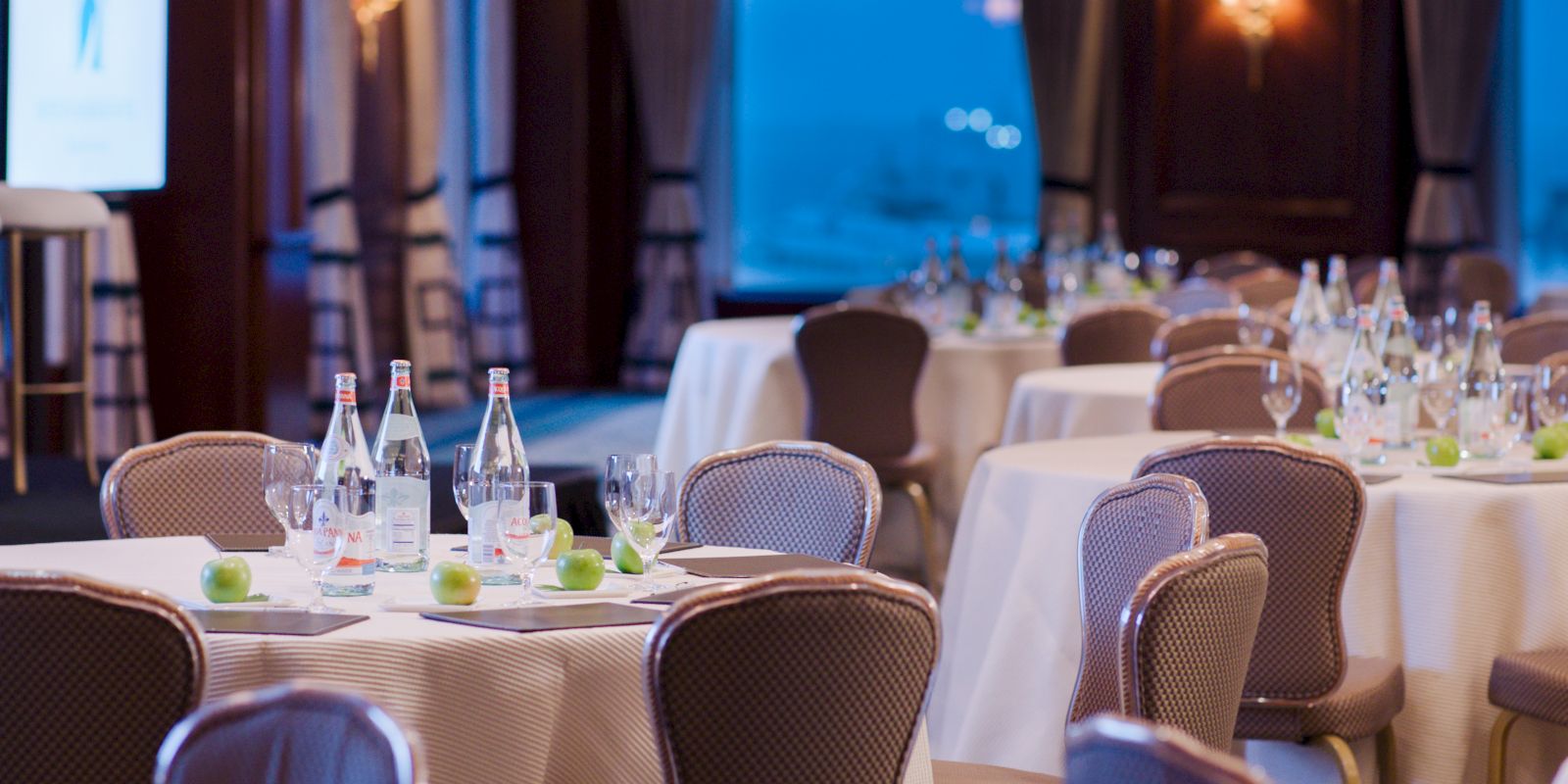 Elegant dining room setup with tables, chairs, glasses, and bottles, ready