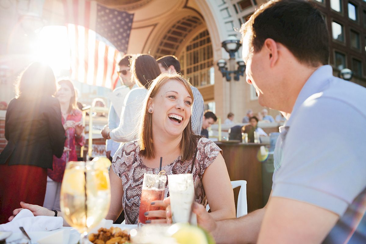 Two people are enjoying a conversation at an outdoor dining setting with drinks on the table.