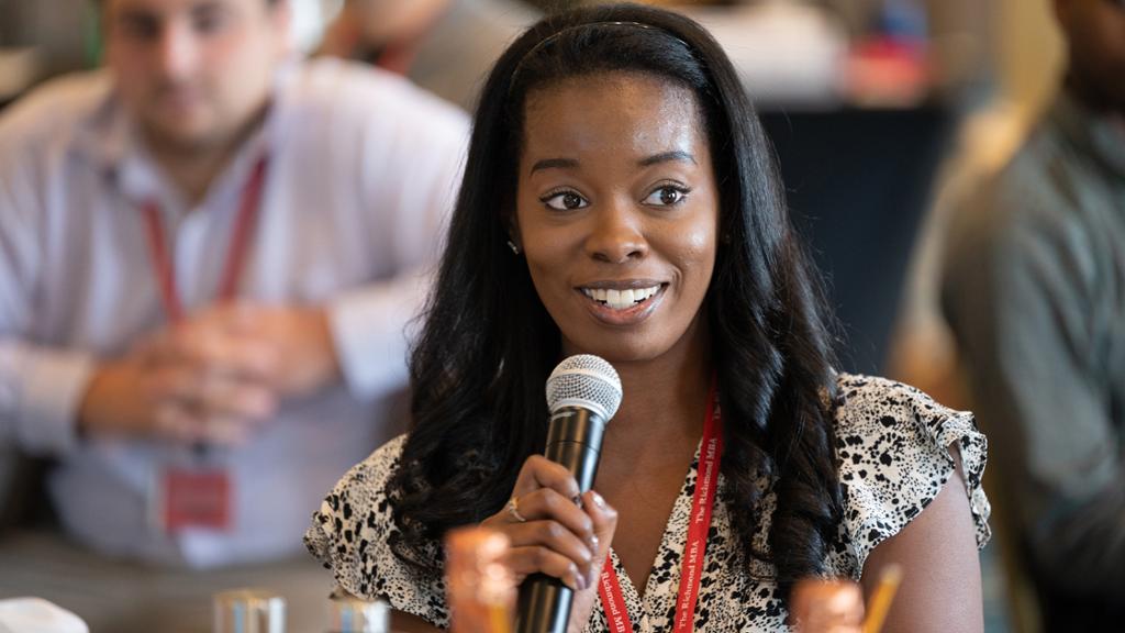 A Richmond MBA student holds a microphone and speaks at an event.