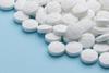 A close-up photograph of a pile of white aspirin pills on a blue paper background