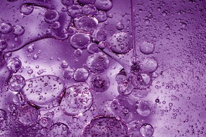 A close-up, full-frame image of bubbles of different sizes in a purple liquid