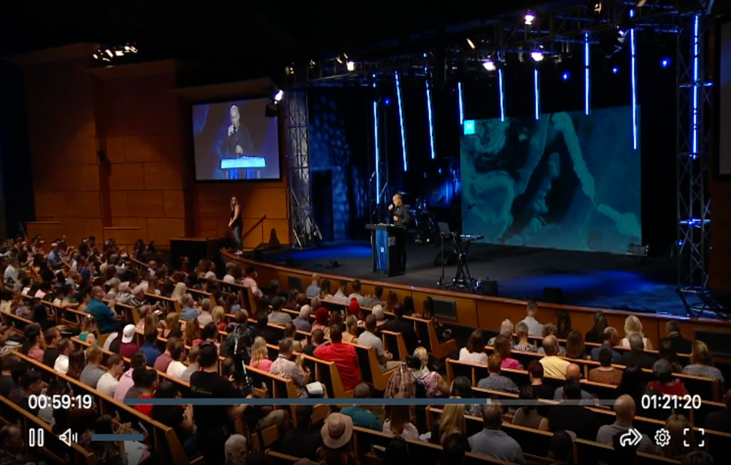 Screenshot of video broadcast from Harvest Ministry depicting a large audience enjoying a religious service.