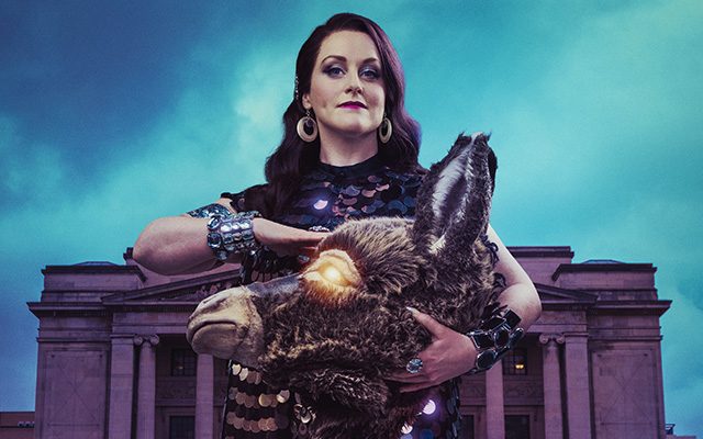 A woman holding a donkeys head in front of a building with columns.