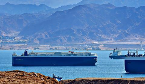 Large ships sailing past an arid, mountainous landscape