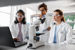 science research, work and people concept - international team of scientists with laptop computer and microscope working in laboratory