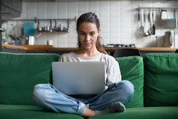 Serious woman using laptop checking email news online sitting on sofa, searching for friends in internet social networks or working on computer, writing blog or watching webinar, studying at home