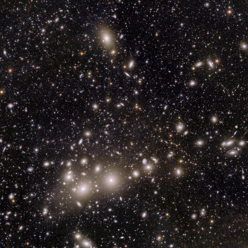 The image shows thousands of galaxies across the black expanse of space. The closest thousand or so galaxies appear as small disks of spiraling material, surrounded by halos of yellow and white light.