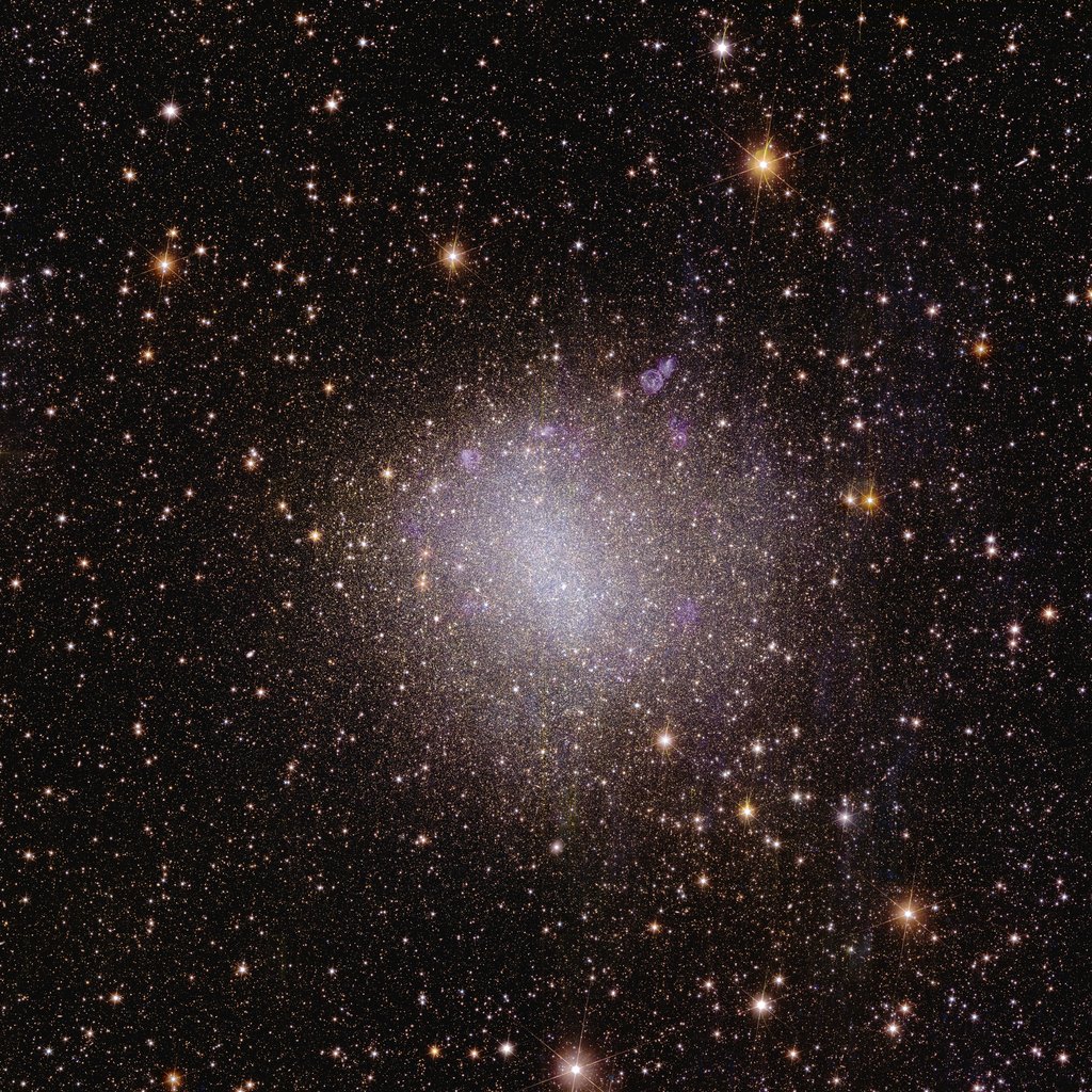 This square astronomical image is speckled with numerous stars visible across the black expanse of space. Most stars are crowding the center of the image and form an irregular blob.