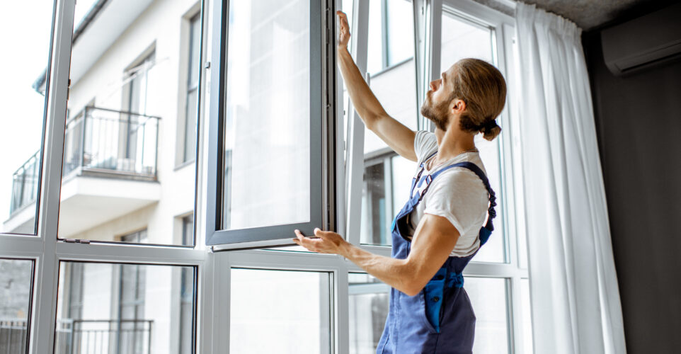 Workman in overalls installing or adjusting plastic windows in the living room at home