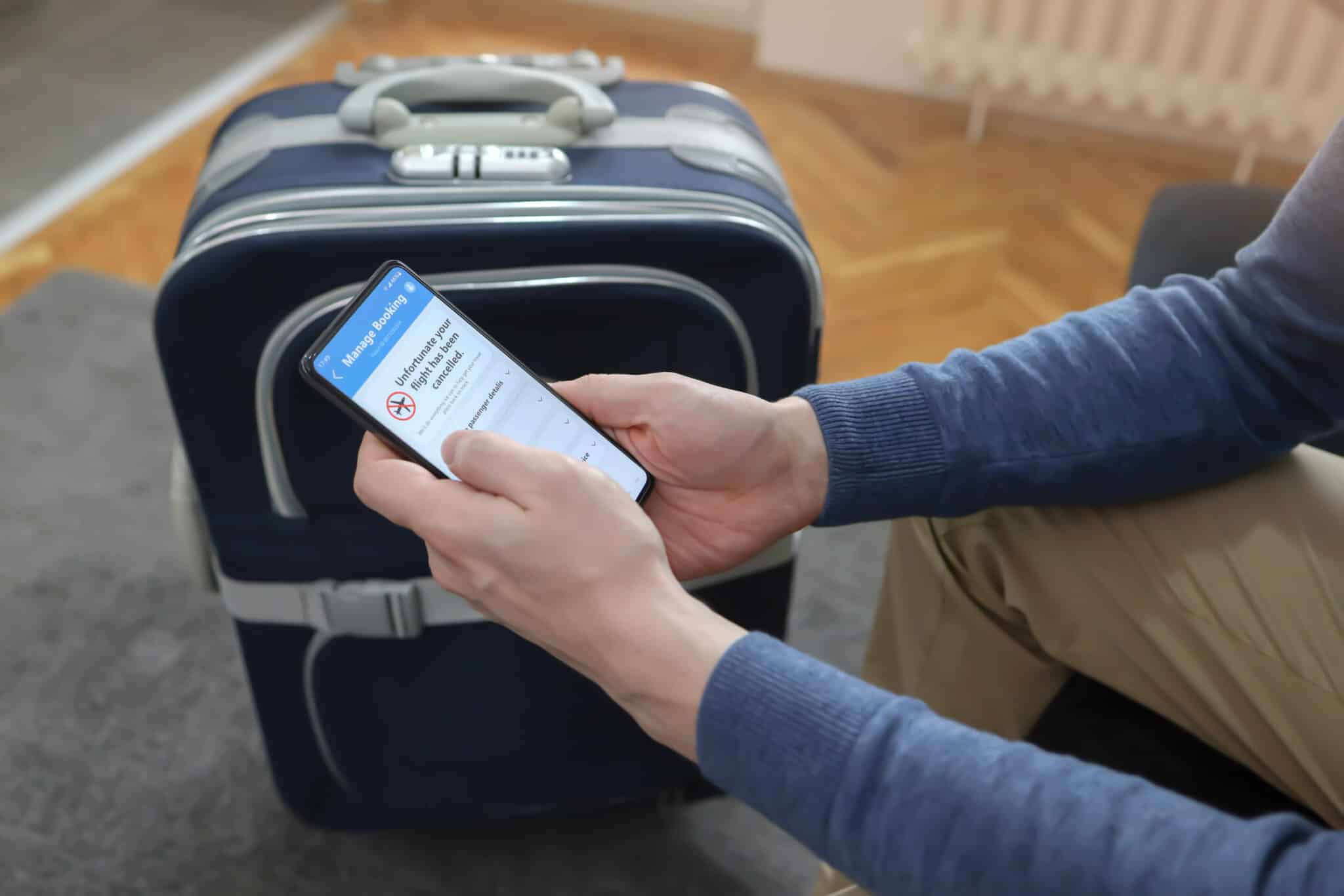 Man looking at a cancelled booking information with luggage in the background