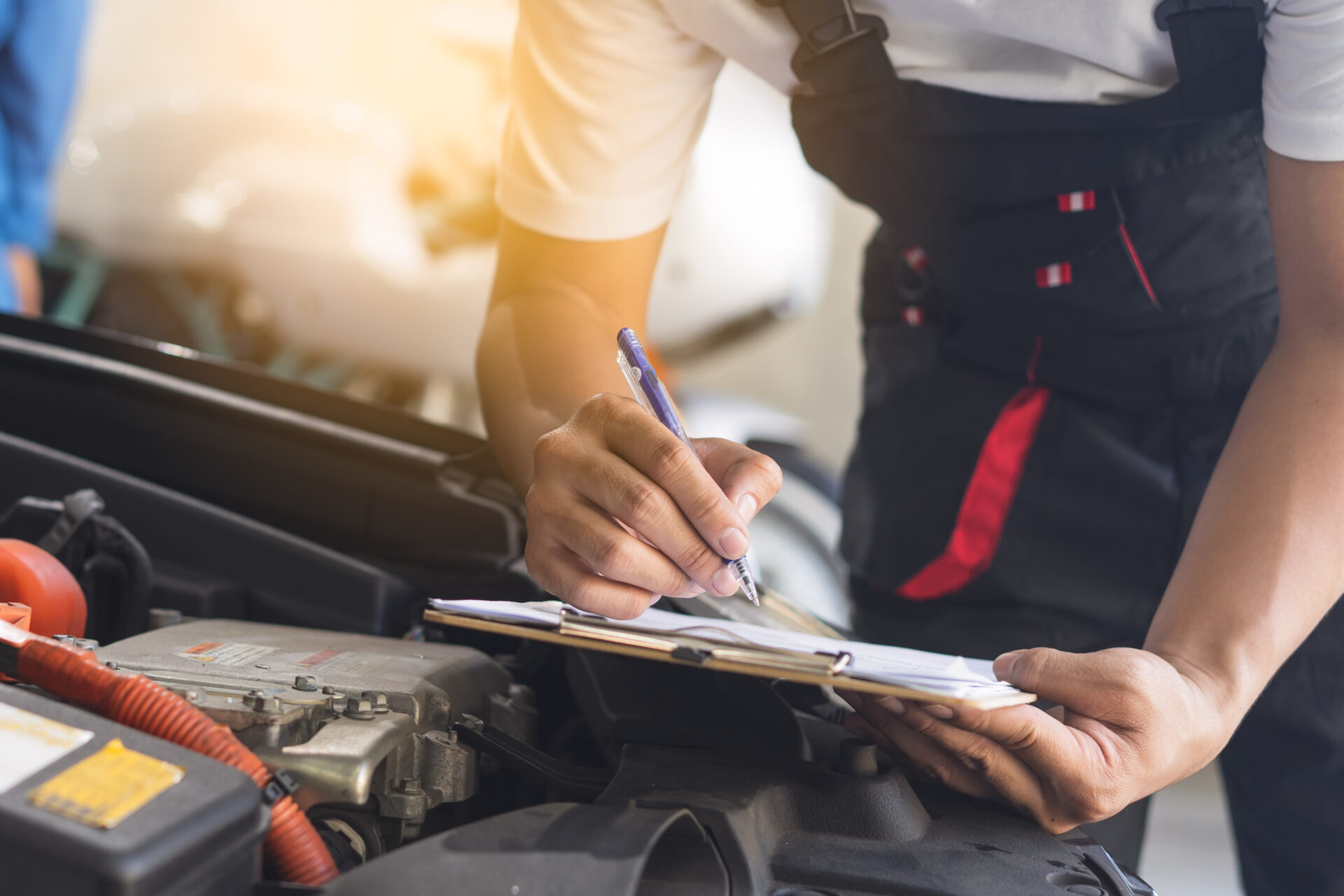 Mechanic working on car motor with clipboard