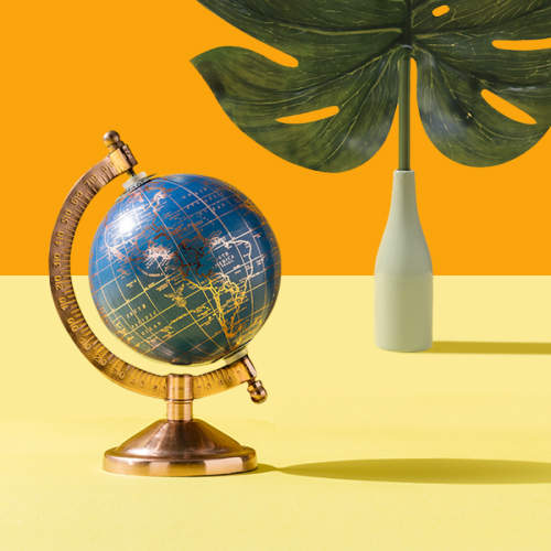 A antique globe resting on a yellow surface and vase with a large, tropical leaf.