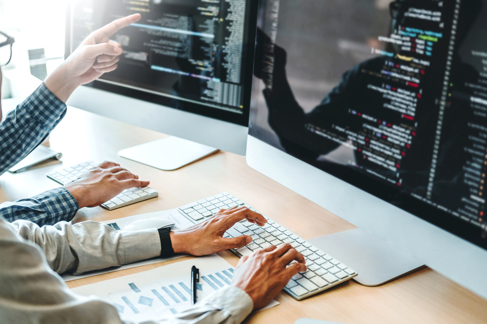 Dos personas trabajan en sendos ordenadores y en la pantalla aparecen software para empresas.