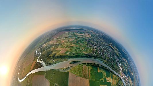 Aerial view from high altitude of little planet earth with small village houses and distant green cultivated agricultural fields with growing crops on bright summer evening