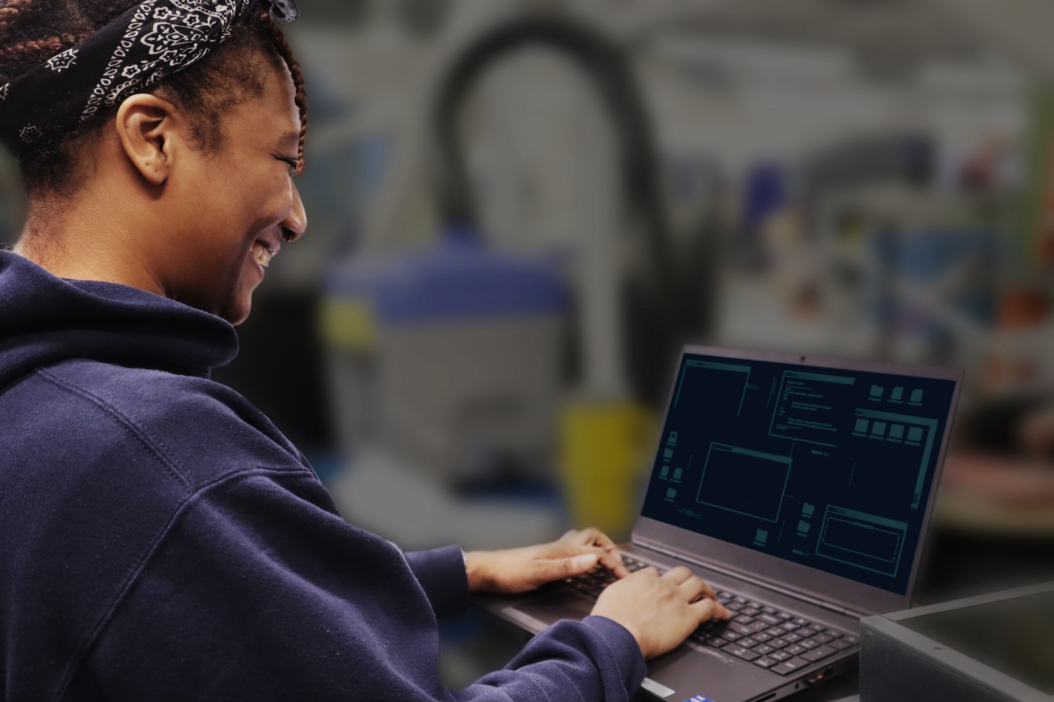 The side profile of a Blue Origin employee wearing a hoodie shows them smiling at a laptop screen with their hands on the keyboard.