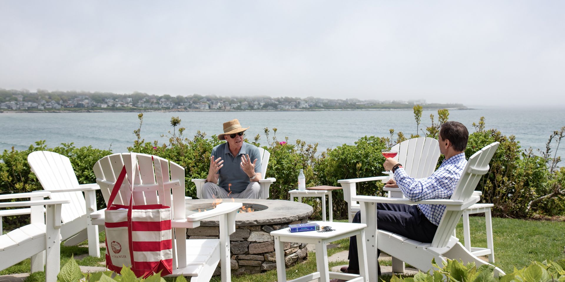 A Couple Of Men Sitting At A Table With A Body Of Water In The Background