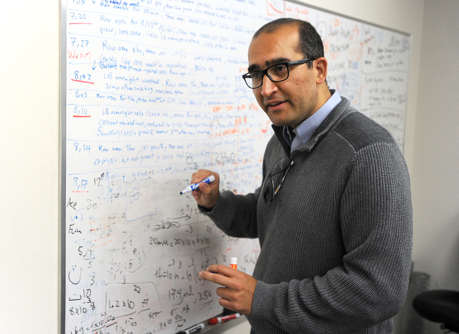 Moh El-Naggar, an assistant professor of physics at the University of Southern California, stands at the grease board where he and his team brainstorm ideas about their work involving biological electron transport. El-Naggar and other scientists at USC are doing basic research to determine how certain bacteria are able to transfer electrons great distances from themselves to other cells or inorganic minerals. Photograph by Kent Treptow for PBSNewsHour