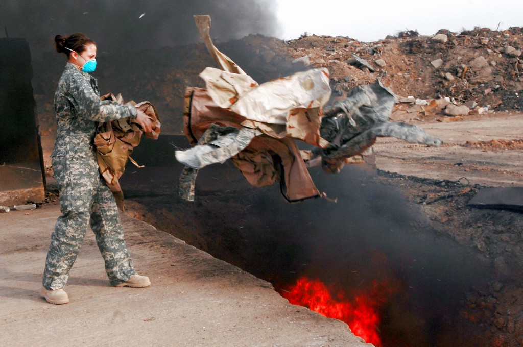 Senior Airman Frances Gavalis tosses unserviceable uniform items into a burn pit March 10 at Balad Air Base, Iraq. Military uniform items must be burned to ensure they cannot be used by opposing forces, according to the U.S. military. Photo by U.S. Air Force/Senior Airman Julianne Showalter